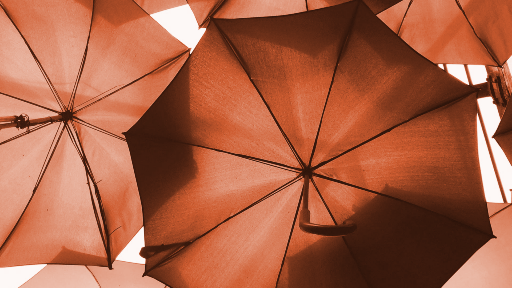 Close-up view of overlapping open umbrellas seen from below, showing their spokes and fabric panels against the light. Hallett Financial Solutions